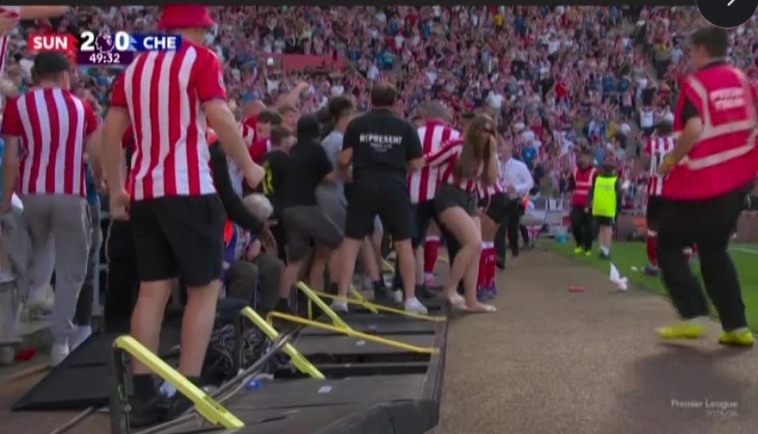Sunderland fans celebrating on the field, wearing red and white striped jerseys, surrounded by security.