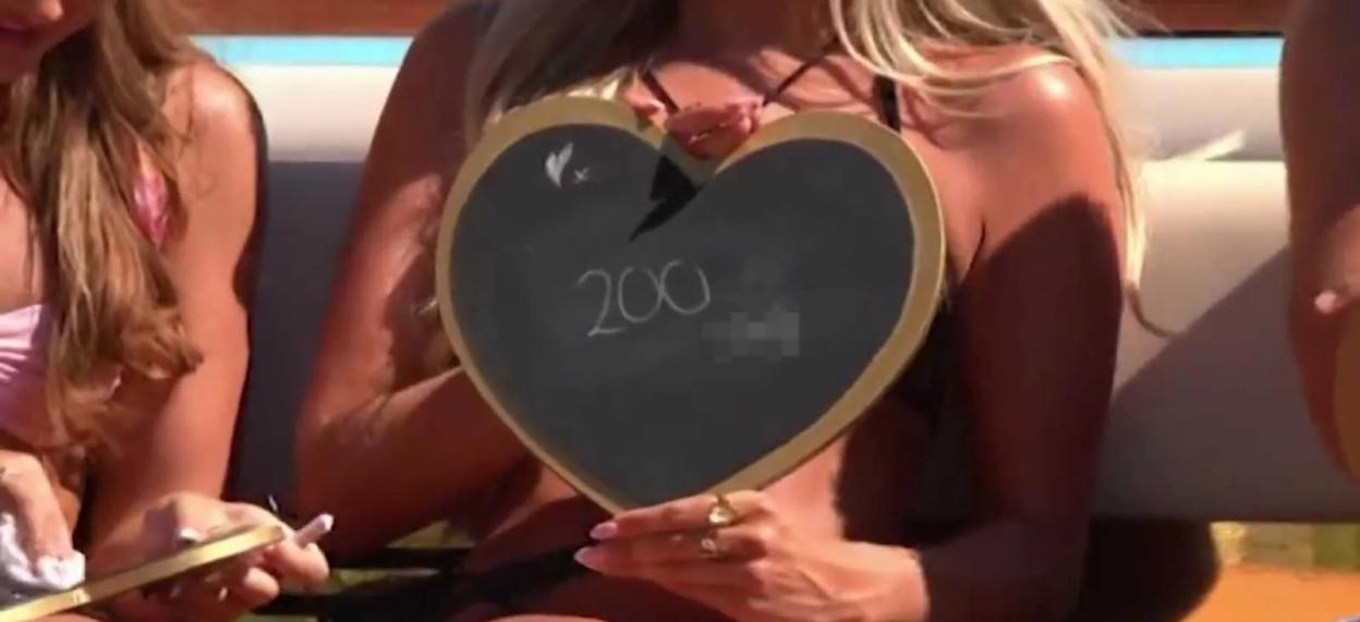 A woman holds a heart-shaped chalkboard displaying the number "200," with a title about "Love Island All Stars" and a contestant claiming to have slept with over 130 women.