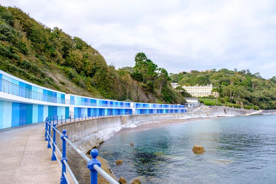 Meadfoot Bay, Torquay, with blue beach huts and lush hills.