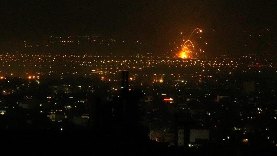 Night view of a city with an explosion of light in the distance.