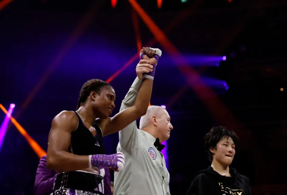 A female boxer raises her arm in victory as a referee holds it up.