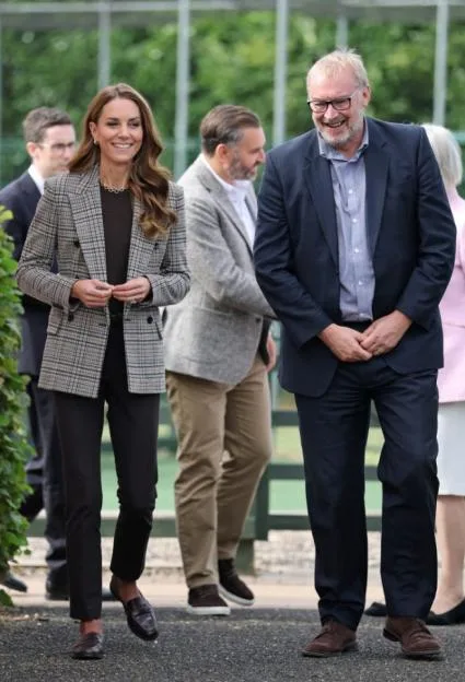 The Princess of Wales smiles as she stands next to a man in a suit, with other people in the background.