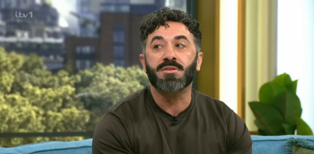 A man with dark curly hair and a beard looks to the right.