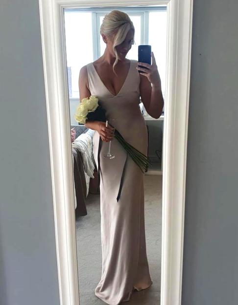 Pamela Pritchard, a blonde woman in a champagne-colored dress, holding a bouquet of white roses and a champagne flute, takes a mirror selfie.