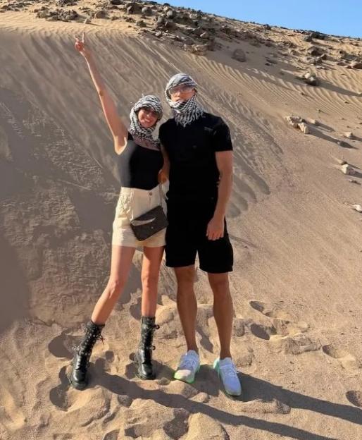 Two people in keffiyeh head coverings posing on a sand dune.