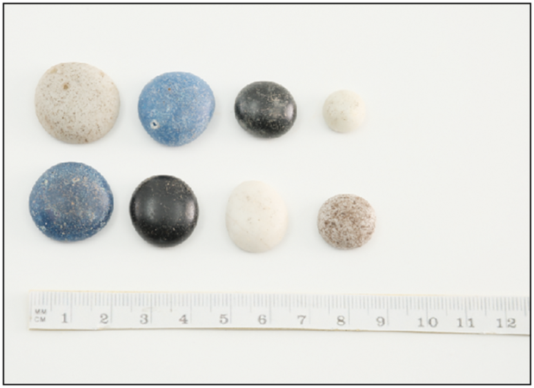 An array of small, round, and flat stones in blue, black, and white, with a ruler underneath.