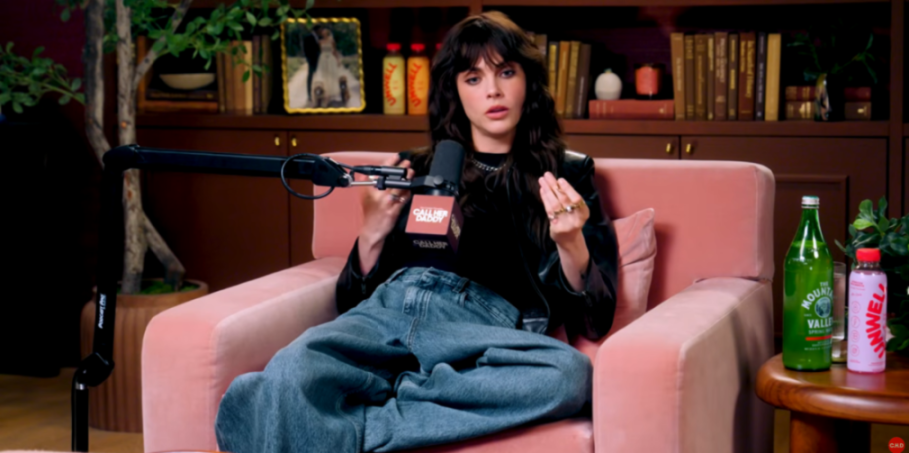 Woman in a black leather jacket and wide-leg jeans speaking into a microphone with the "Call Her Daddy" logo.