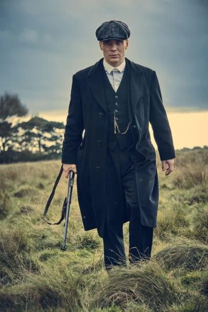 Thomas Shelby walks through a field carrying a shotgun.