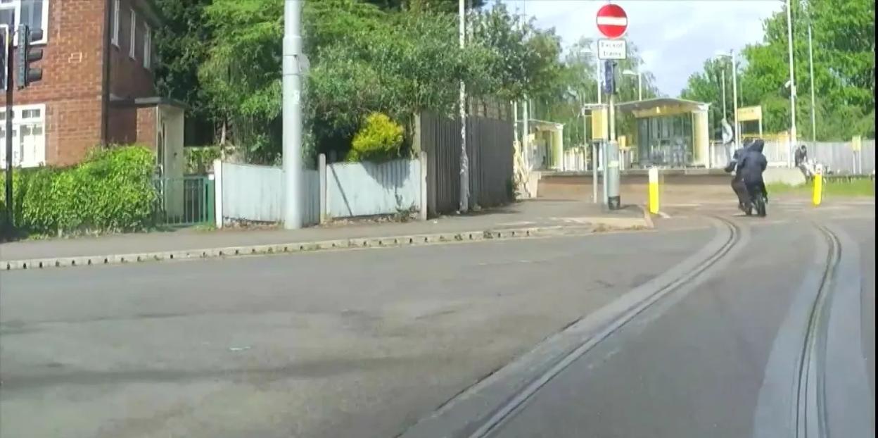 Two individuals on an e-bike are pursued by a police vehicle down tram tracks.