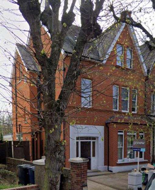 A brick house with white trim in Avenue Crescent, Acton, behind a large tree.