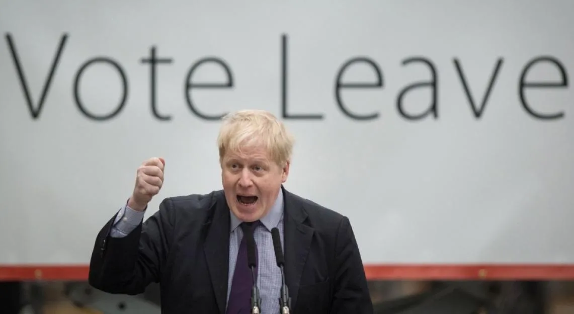 Boris Johnson speaking at a Vote Leave rally, raising his fist in front of a banner.