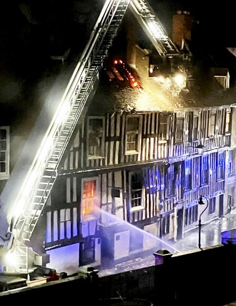 Firefighters battling a blaze at a historic building with flames visible on the roof and water being sprayed onto the exterior.