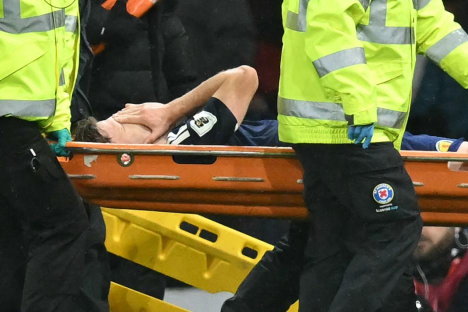 A footballer on a stretcher being carried off the field by medical personnel.