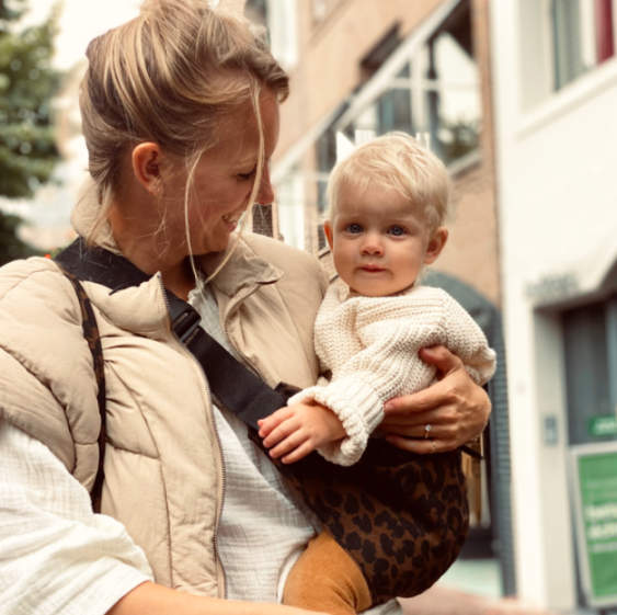 A woman holding a baby in a leopard print carrier.