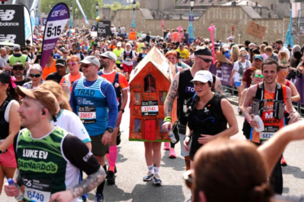 A person in a house costume during a marathon, surrounded by other runners.