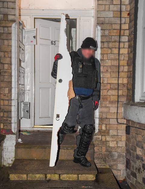 A police officer in tactical gear carries away a broken door from an address during a raid.
