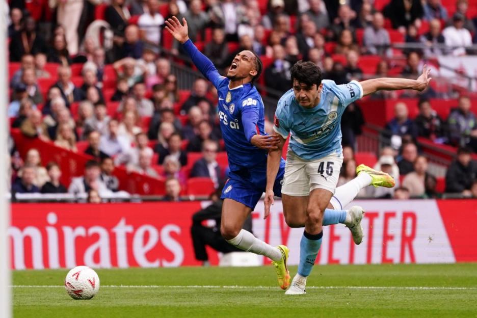 A Chelsea player in blue reaching out for a foul as a Manchester City player in light blue runs past him.