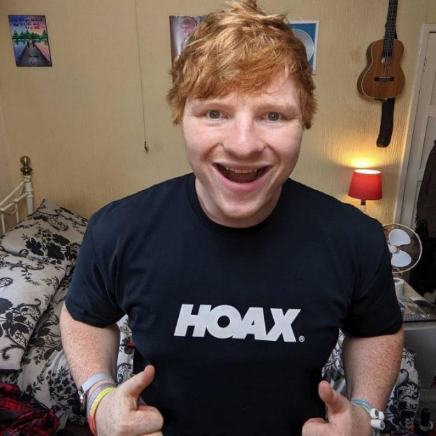 Man with red hair wearing a "HOAX" t-shirt giving two thumbs up.