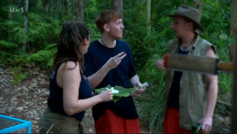 Three individuals conversing while holding food in a jungle environment.
