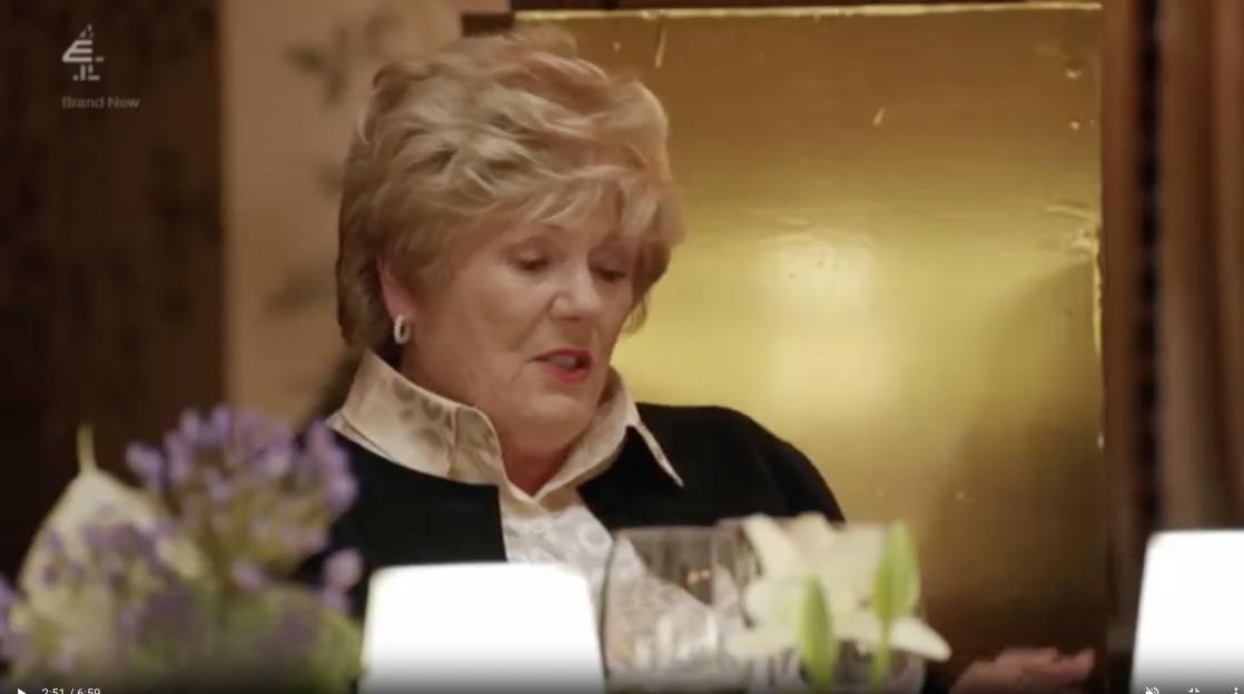 Older woman talking at a dinner table.