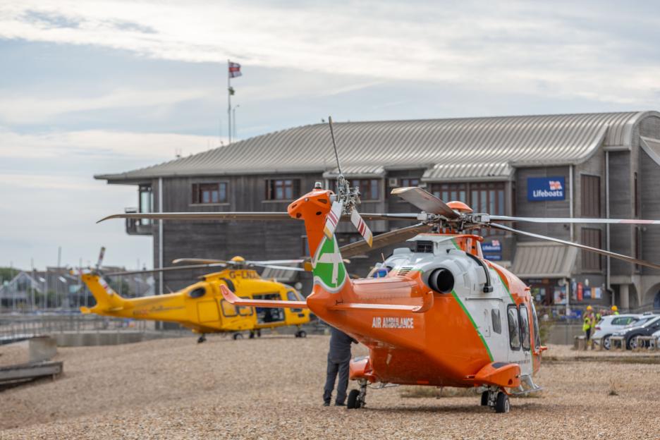 Two air ambulances, one orange and one yellow, are on the ground at Shoreham Lifeboat station.