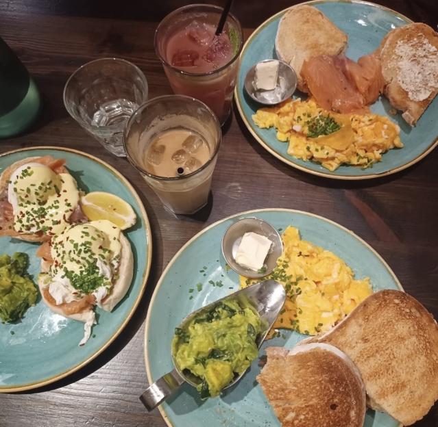 Brunch plates with Eggs Benedict, smoked salmon, scrambled eggs, avocado, and drinks.