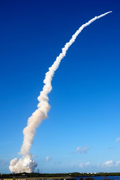 NASA's Artemis II moon rocket lifting off from Kennedy Space Center, leaving a thick trail of white smoke against a clear blue sky.