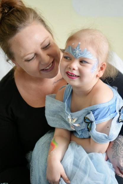 Primrose Hocking, a young child with face paint, sits on an adult's lap.