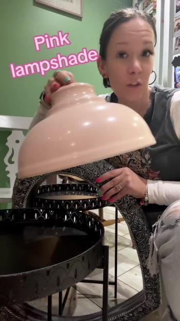 A woman holding a pink lampshade above a decorative mirror.