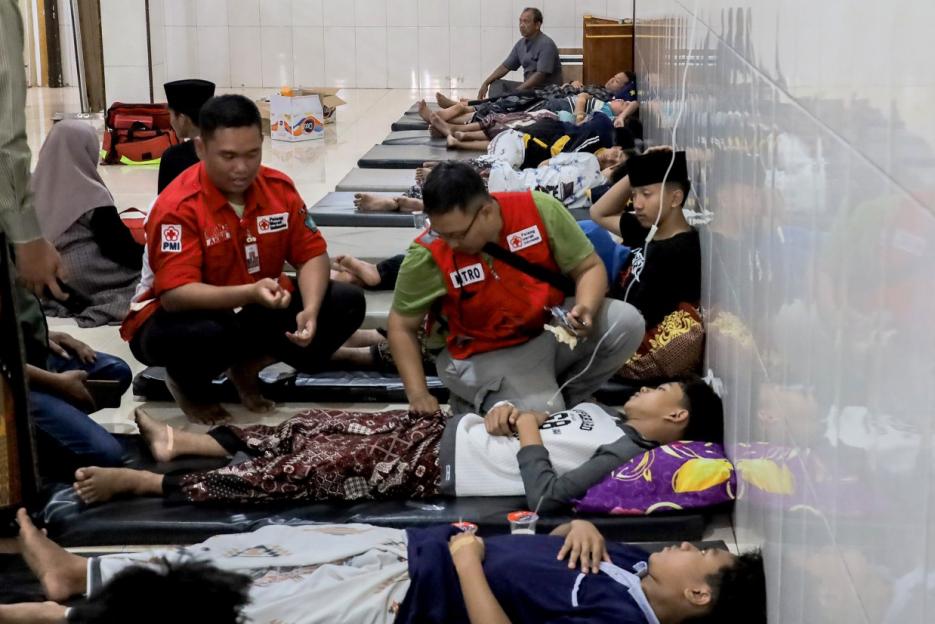 Students on mats receiving aid from volunteers after suspected food poisoning.