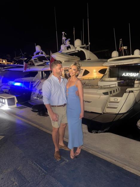 Ashley Dommett and his girlfriend posing by yachts at night.