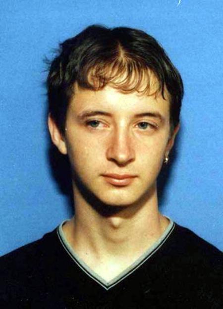 Headshot of a young man with short dark hair and light eyes against a blue background.