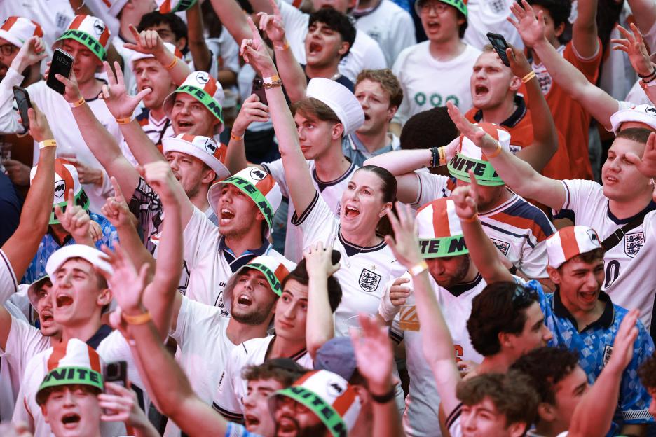 England supporters cheer with hands raised, wearing team jerseys and bucket hats with the word "UNITE."