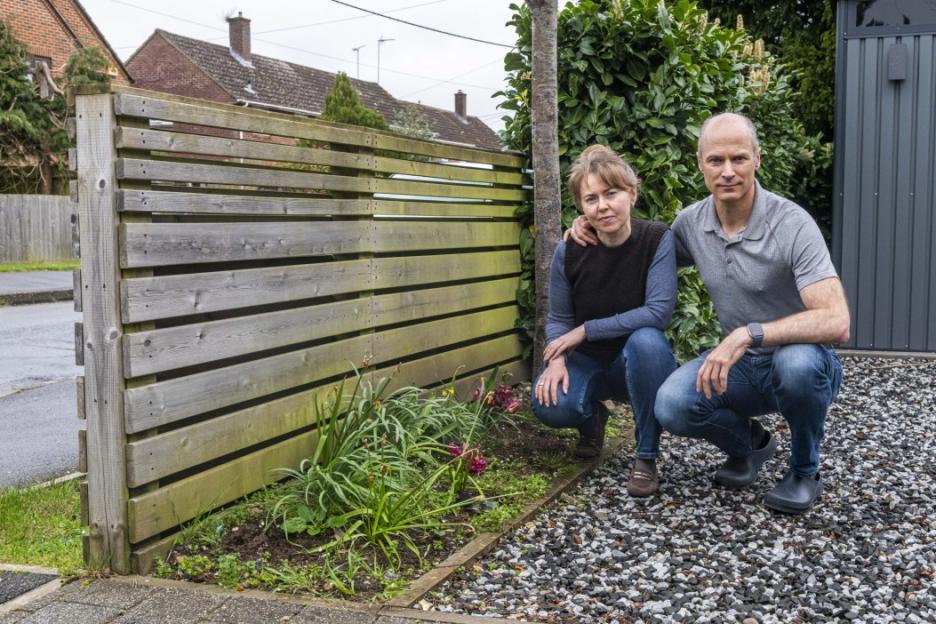 A man and a woman squatting next to a wooden fence with plants in front of them.