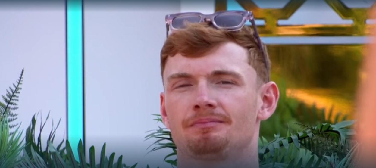 A man with ginger hair and a beard, wearing sunglasses on his head, smirking at the camera.