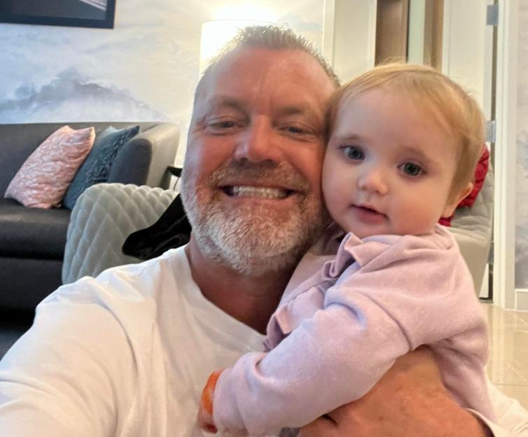 A man in a white t-shirt holding a baby in a pink shirt.