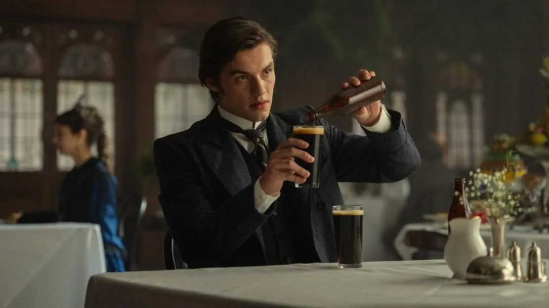 A man wearing a suit pouring a drink into a glass at a table in a pub.