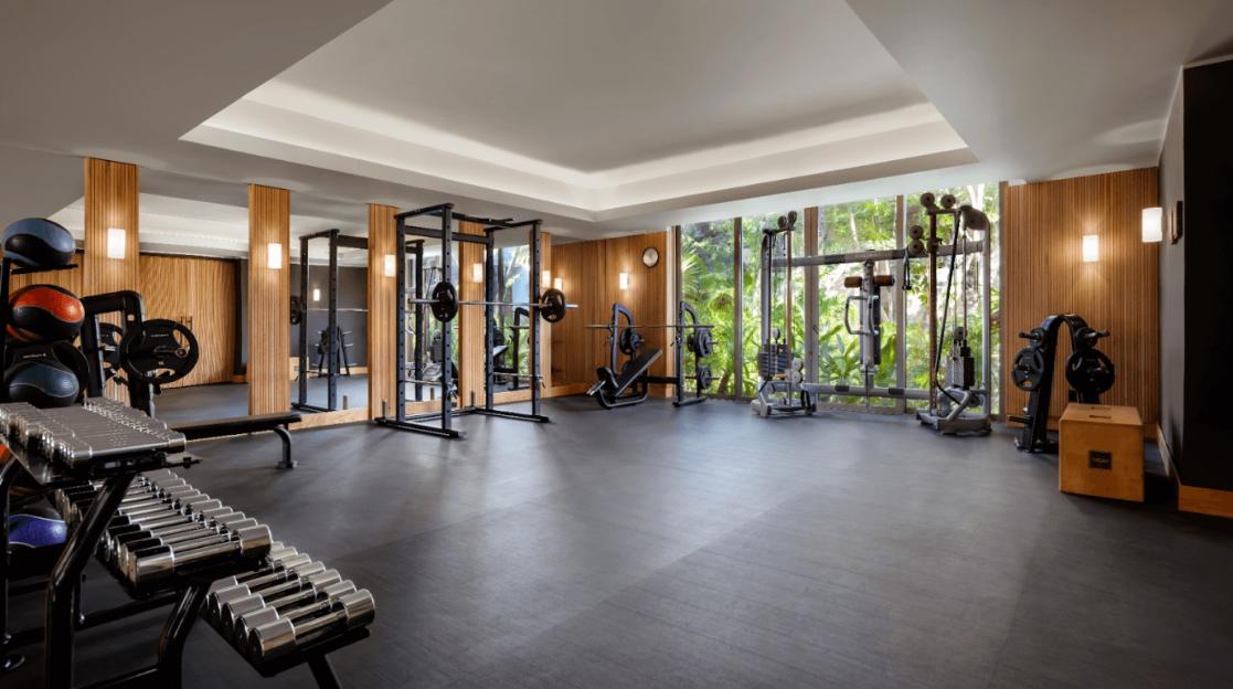 Gym with various exercise equipment and large windows overlooking lush greenery.