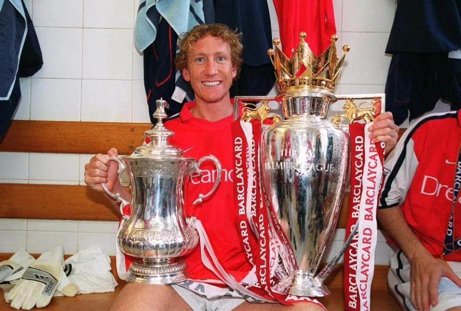 Ray Parlour of Arsenal poses with the FA Cup Trophy and the Premier League Trophy in the locker room.