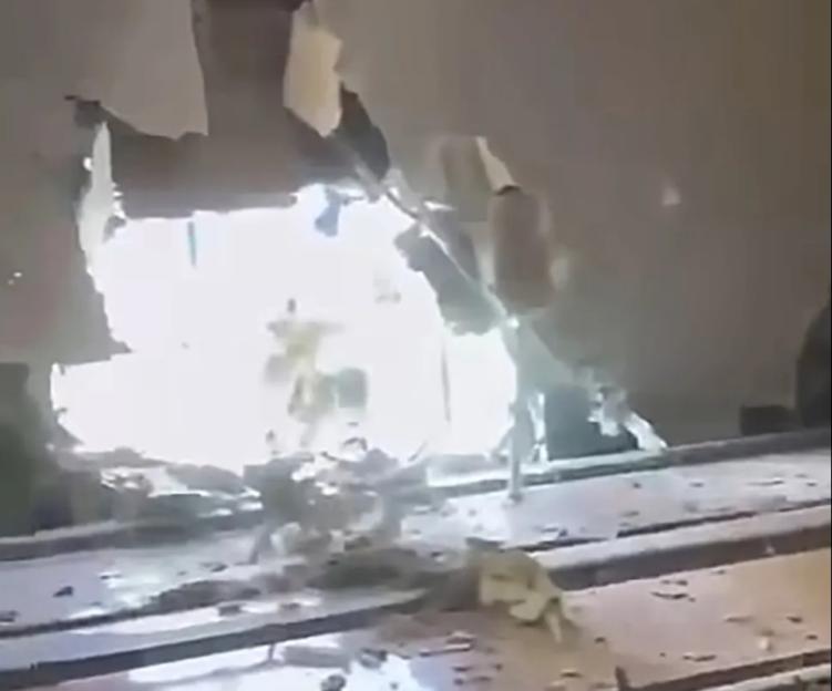 A damaged wall with a large hole, debris on the floor, and bright light showing through the hole.