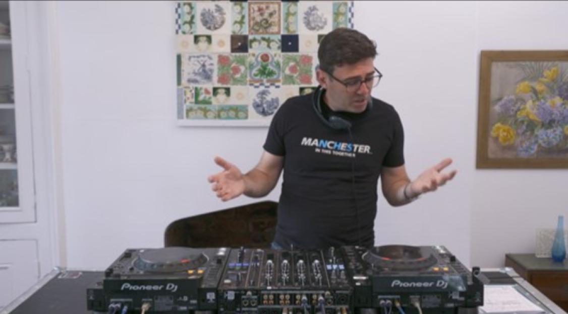 Andy Burnham in a "Manchester. In This Together." t-shirt standing behind DJ decks.