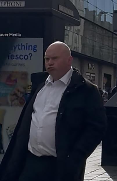Kevin Dean, a bald man in a white shirt and black jacket, with a serious expression.