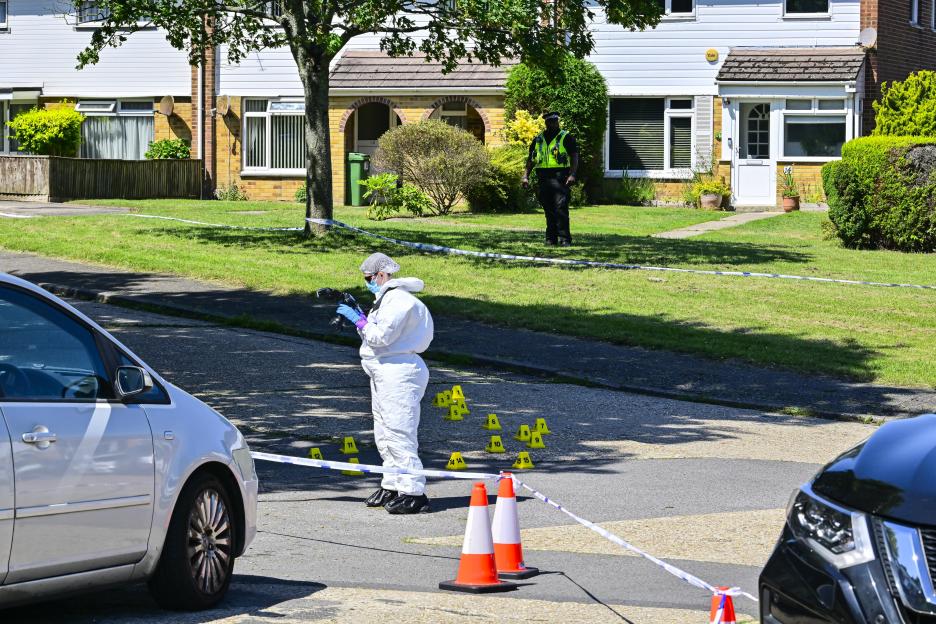A forensic investigator in a white suit photographs evidence markers at a crime scene on Dale Close, Poole.