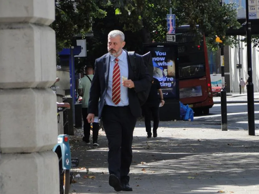 Darren Cooper walks down a city street in a suit and red-and-white striped tie.