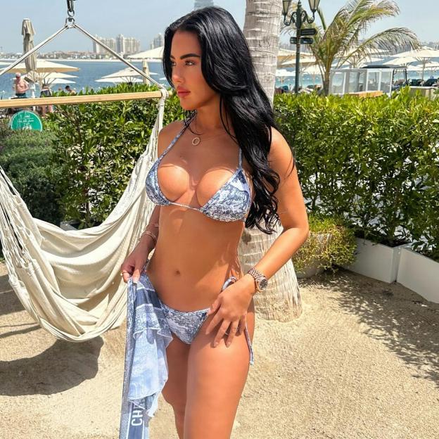 Yazmin Oukhellou in a patterned bikini holding a matching sarong on a sandy beach.