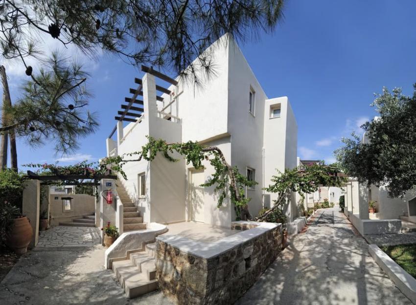 The Jardin Milenio Hotel features white buildings with stairs and a walkway, shaded by trees and vines.