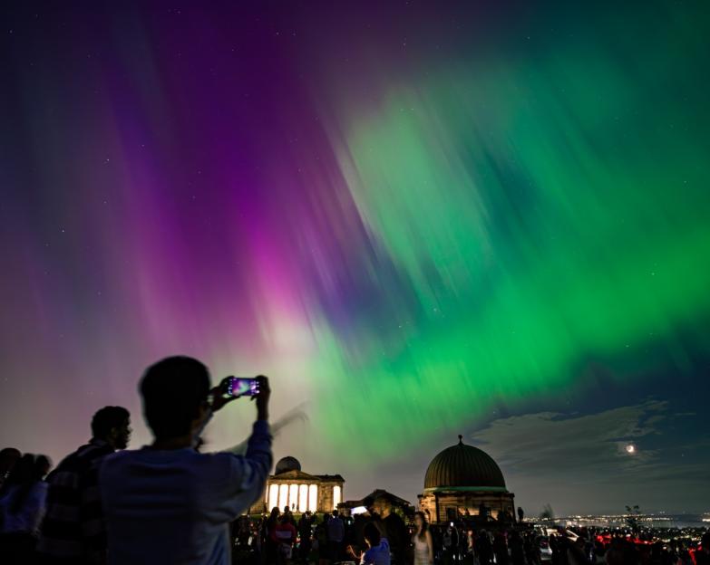 Spectators on Calton Hill capturing stunning northern lights on smartphones during a geomagnetic storm in Edinburgh.
