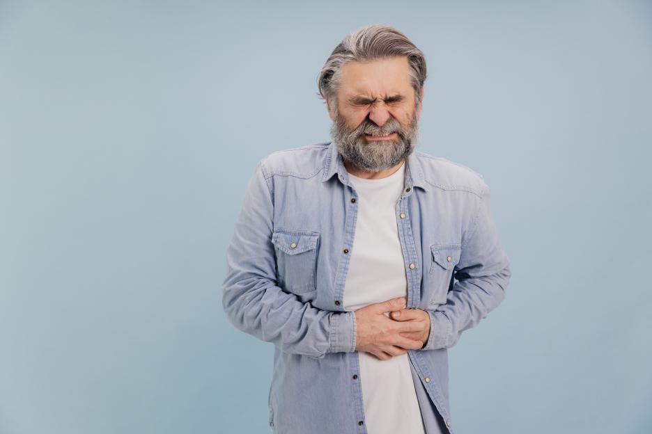 Senior man grimacing from abdominal pain and holding his stomach.