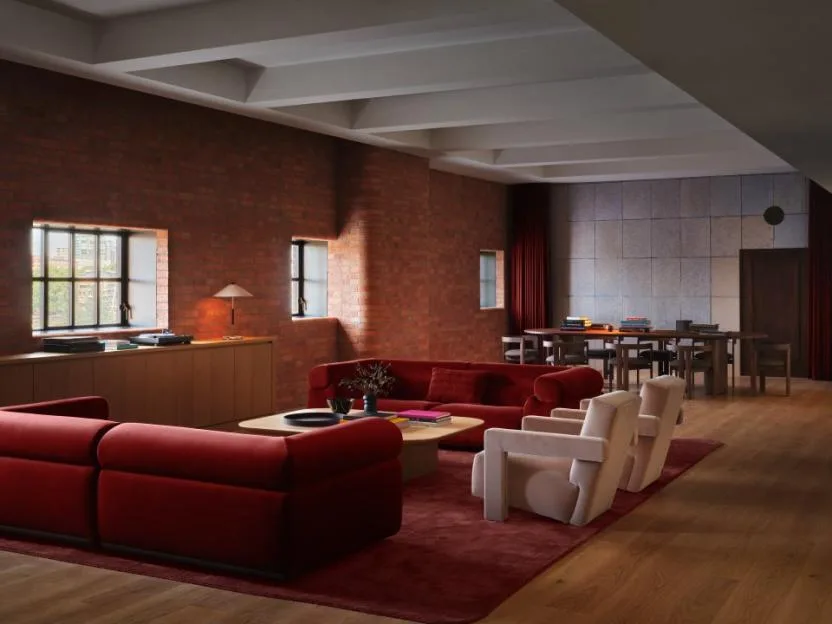 A modern lounge with red brick walls, red couches, and a large dining table.