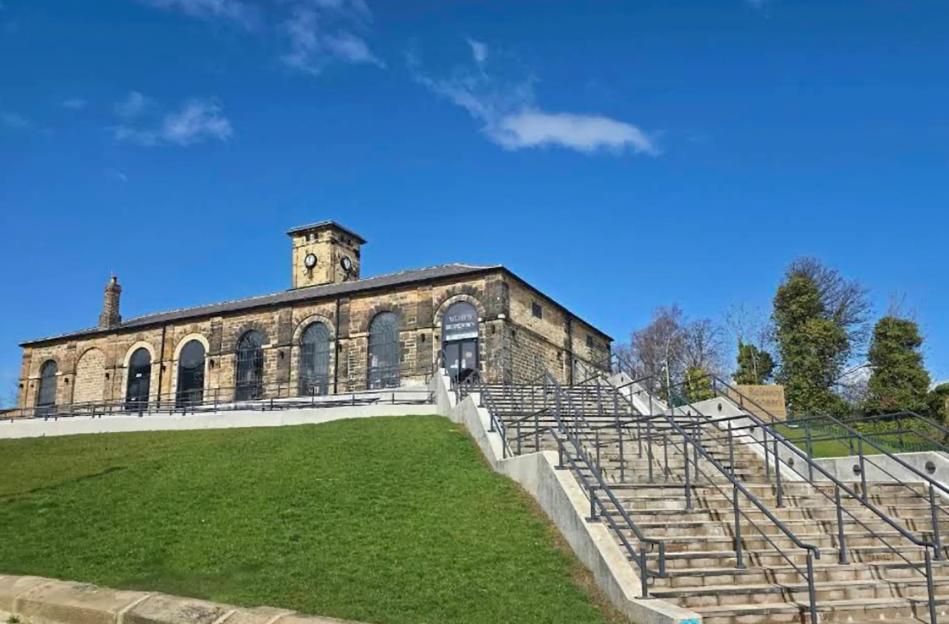 Hopetown Darlington Museum, a stone building with a clock tower and arched windows, atop a grassy hill with wide stairs leading up to it.